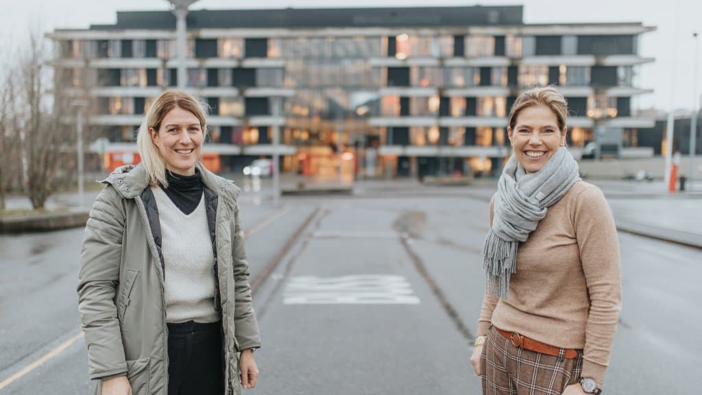 Foto av to kvinner som står foran en skolebygning.