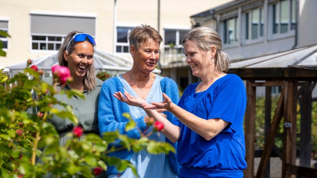 Foto av tre kvinner som står sammen utenfor en bygning. De både smiler og ler sammen.